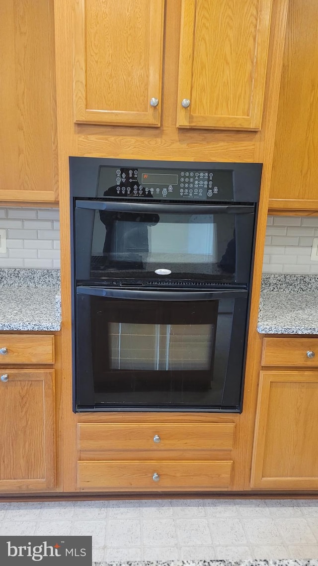 details featuring light floors, light stone counters, decorative backsplash, and dobule oven black