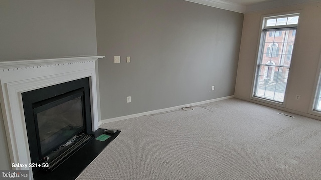 unfurnished living room featuring baseboards, visible vents, a fireplace with flush hearth, ornamental molding, and carpet flooring