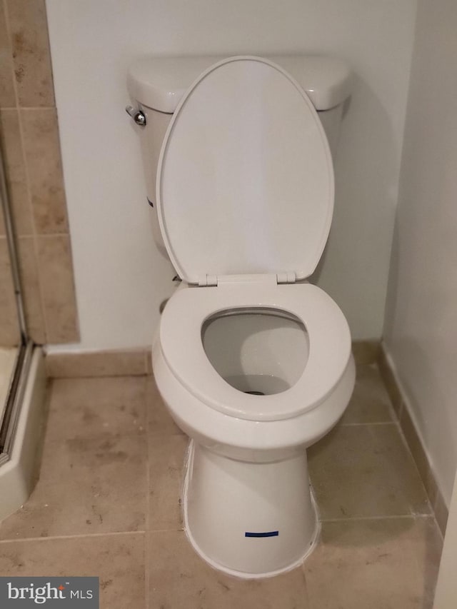 full bathroom featuring baseboards, a shower with door, and toilet