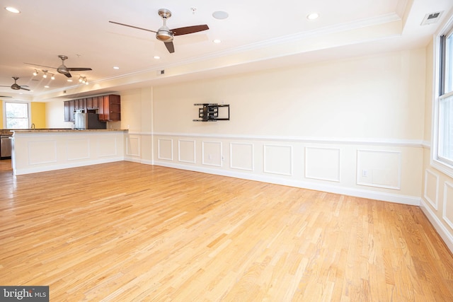 unfurnished living room with visible vents, wood finished floors, a tray ceiling, crown molding, and a decorative wall