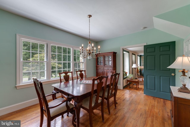 dining area with a chandelier, light wood finished floors, vaulted ceiling, and baseboards