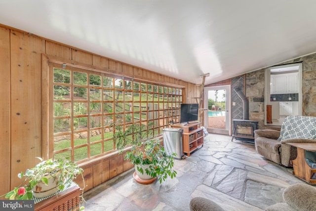 living area featuring vaulted ceiling, wooden walls, a wood stove, and stone flooring