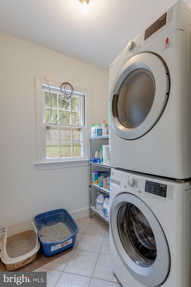 washroom featuring light tile patterned floors, laundry area, stacked washer and dryer, and baseboards