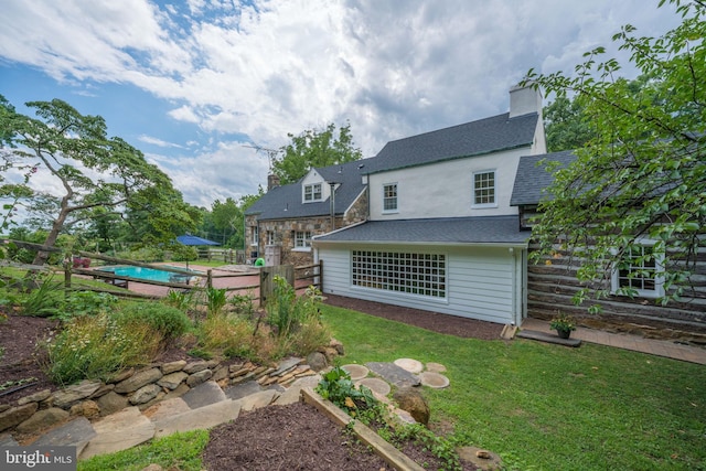 back of house featuring a fenced in pool, a yard, a chimney, a shingled roof, and fence