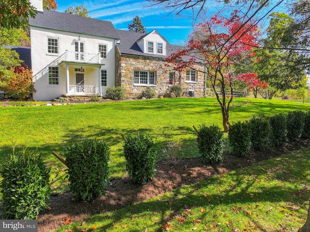 view of front of house featuring a balcony, stone siding, a front lawn, and stucco siding