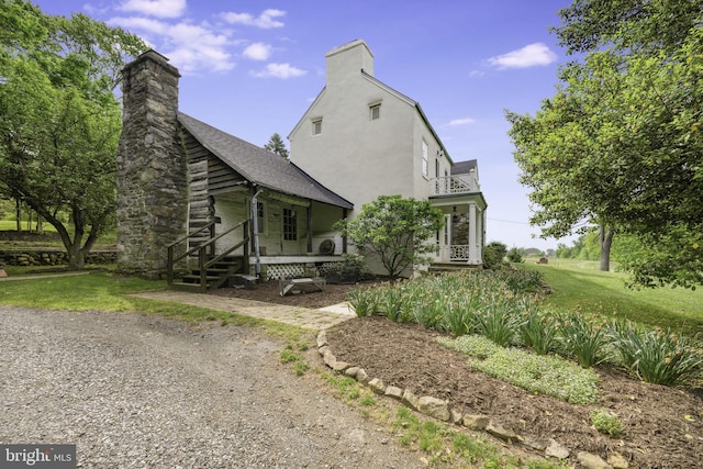 exterior space with a chimney, stucco siding, a porch, a front yard, and a balcony