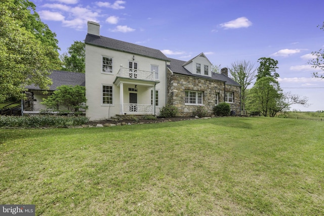 view of front of house featuring a chimney, a front yard, and a balcony