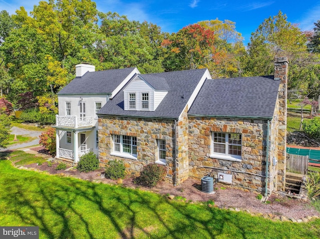 view of front of home with a balcony, central AC, roof with shingles, a front lawn, and a chimney