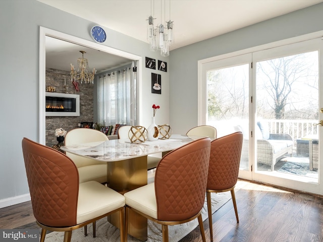 dining area featuring a fireplace, wood finished floors, baseboards, and a chandelier