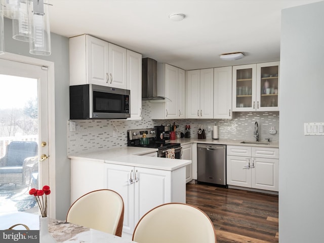 kitchen featuring a sink, backsplash, stainless steel appliances, wall chimney exhaust hood, and white cabinets