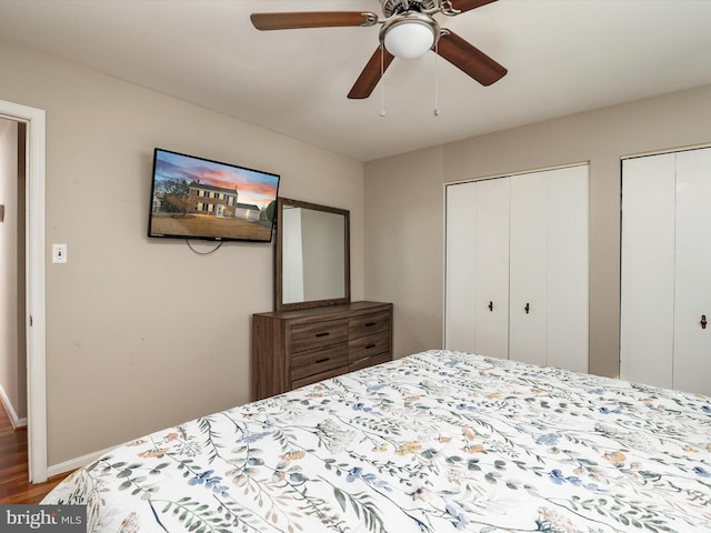 bedroom with wood finished floors, baseboards, two closets, and ceiling fan