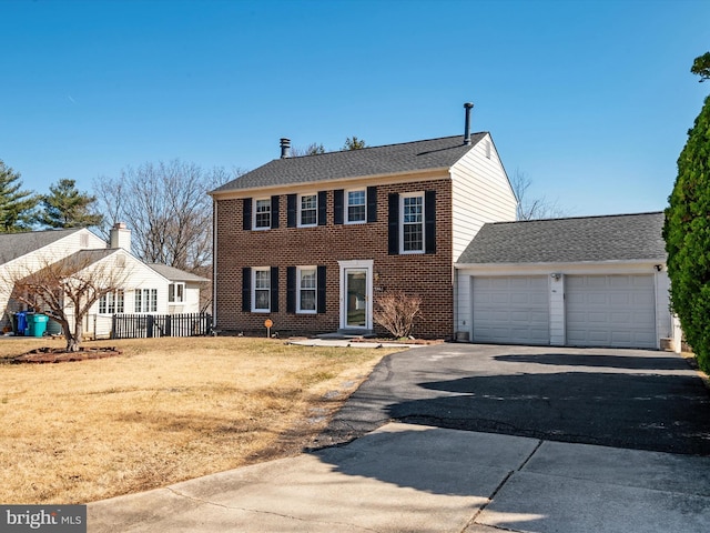 colonial house with fence, a front lawn, a garage, aphalt driveway, and brick siding