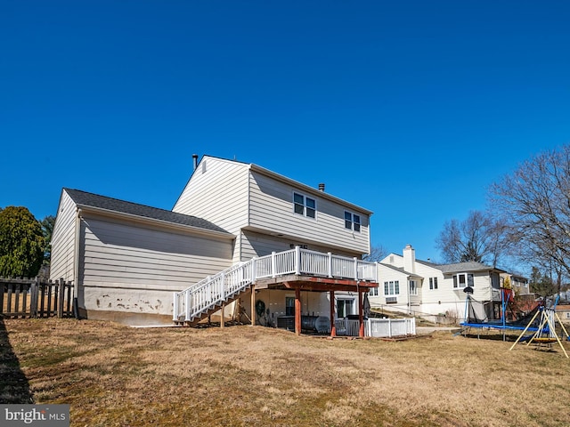 rear view of property with stairway, fence, a deck, a trampoline, and a lawn