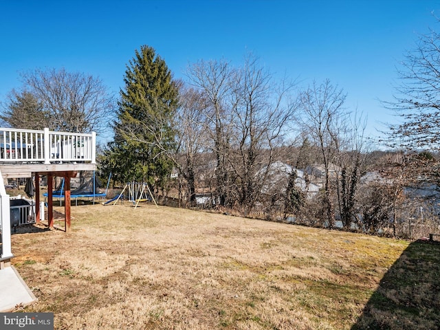 view of yard with a deck, a playground, and a trampoline