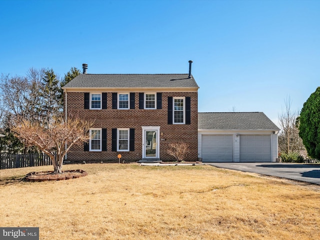 colonial home featuring fence, driveway, an attached garage, a front lawn, and brick siding