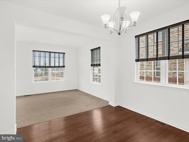 spare room featuring baseboards, wood finished floors, visible vents, and a notable chandelier