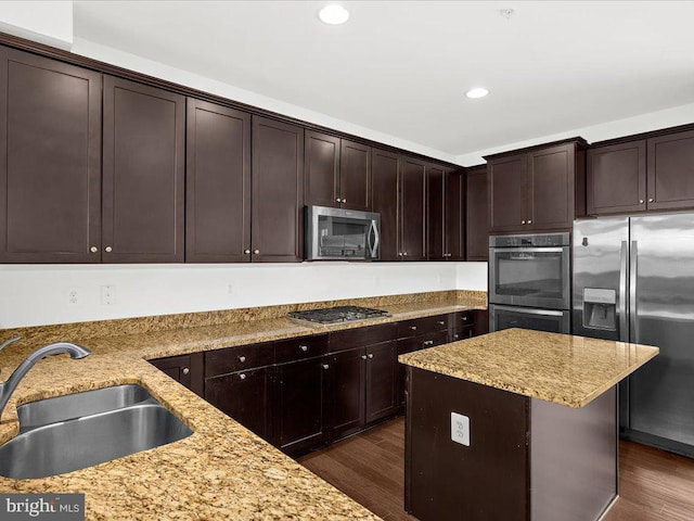 kitchen with dark wood-style floors, appliances with stainless steel finishes, a sink, dark brown cabinetry, and light stone countertops