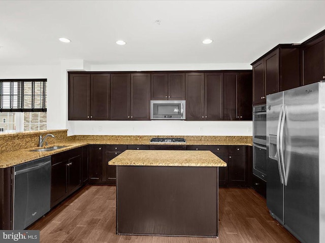 kitchen with dark brown cabinetry, appliances with stainless steel finishes, dark wood-type flooring, light stone countertops, and a sink