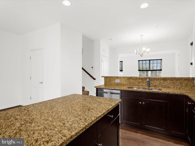 kitchen featuring light stone counters, dark wood finished floors, stainless steel dishwasher, an inviting chandelier, and a sink