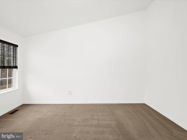 empty room with dark colored carpet, visible vents, and baseboards