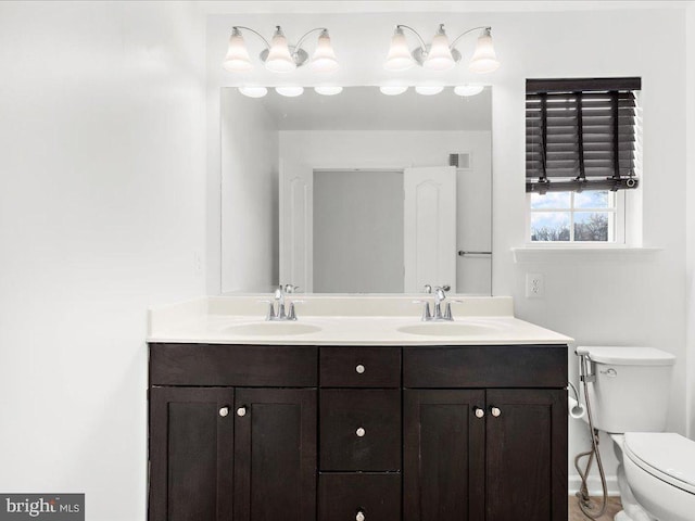 bathroom featuring toilet, double vanity, visible vents, and a sink