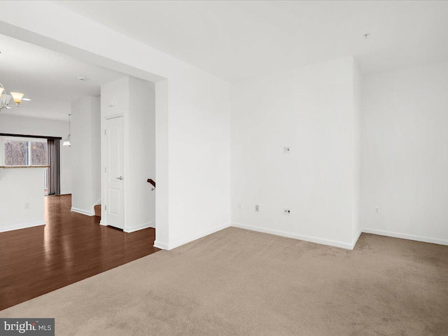 unfurnished room featuring an inviting chandelier, carpet, and baseboards