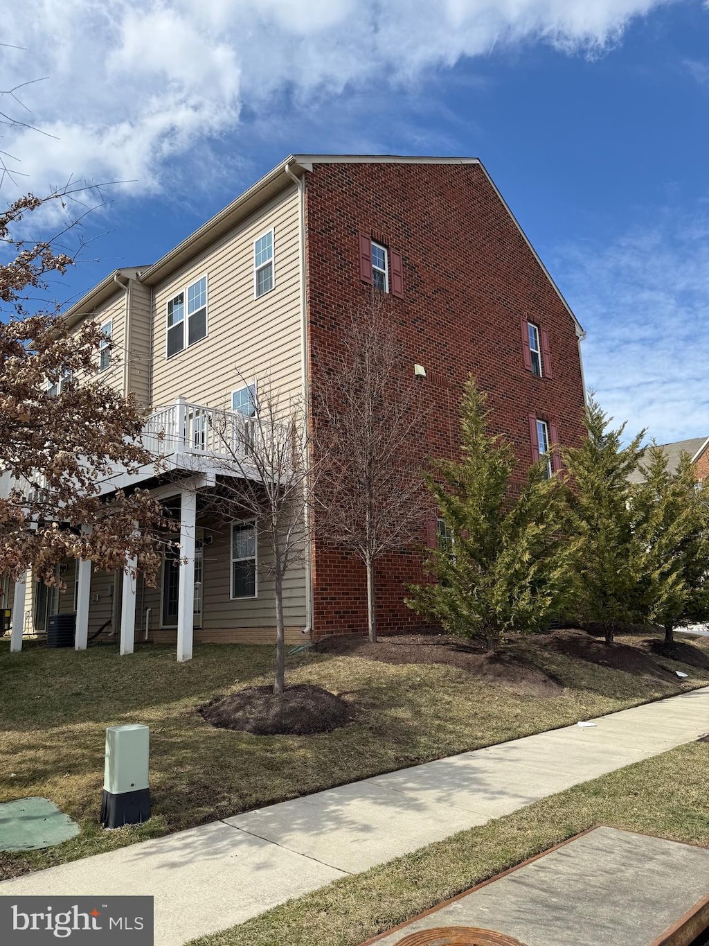 view of side of property with a yard, brick siding, and central AC