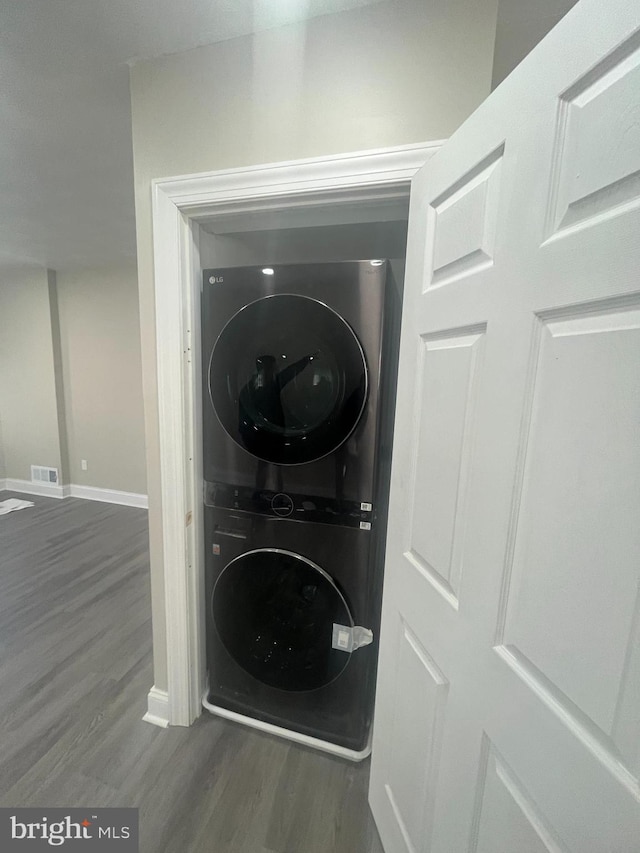 laundry area featuring laundry area, wood finished floors, visible vents, baseboards, and stacked washer / drying machine