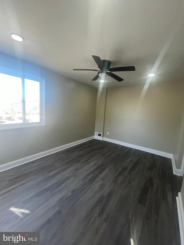 unfurnished room with ceiling fan, dark wood finished floors, visible vents, and baseboards