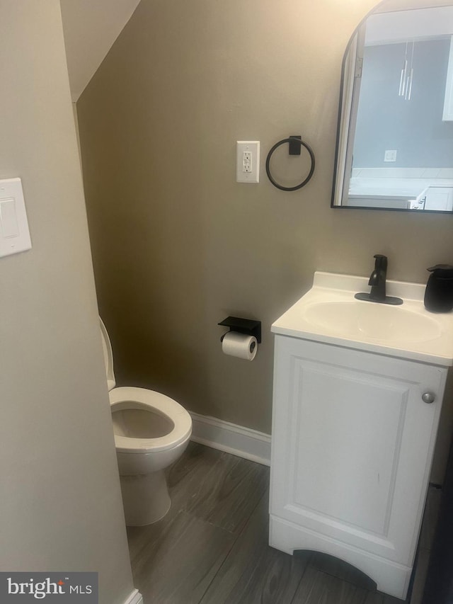 half bathroom featuring toilet, vanity, and baseboards