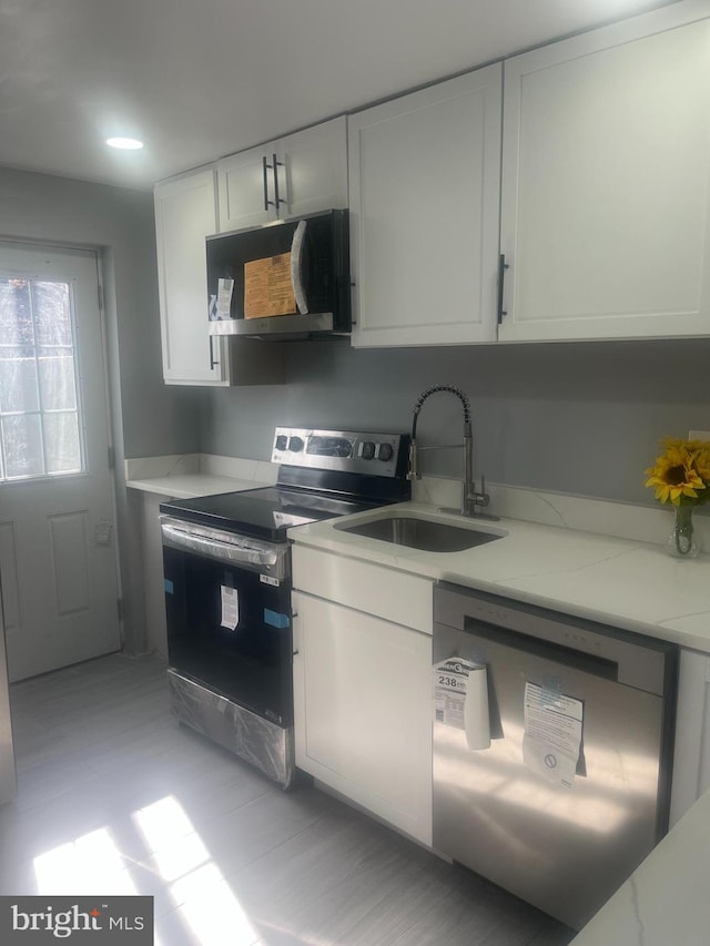 kitchen featuring appliances with stainless steel finishes, white cabinetry, a sink, and light stone countertops