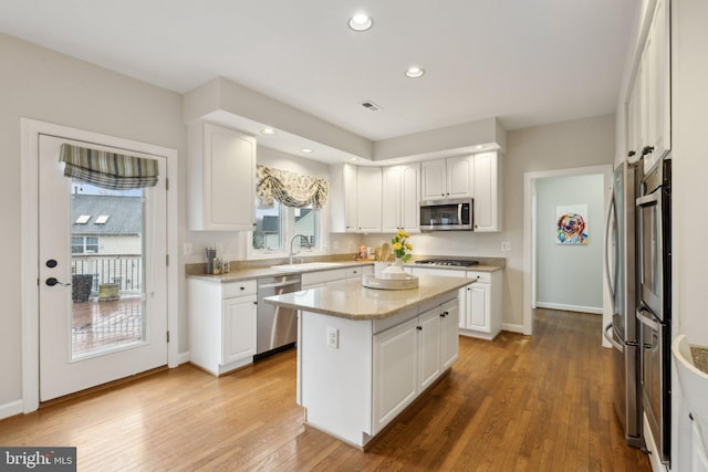 kitchen with stainless steel appliances, a kitchen island, a sink, white cabinetry, and hardwood / wood-style floors