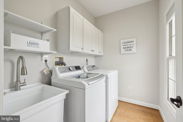 washroom featuring cabinet space, baseboards, light wood-style floors, washing machine and dryer, and a sink