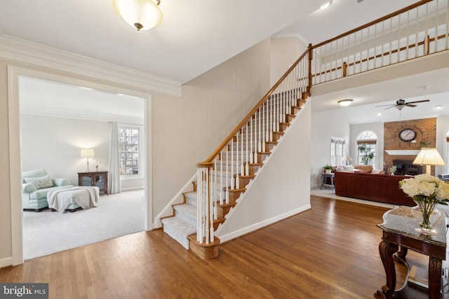 staircase featuring ornamental molding, a fireplace, wood finished floors, and baseboards