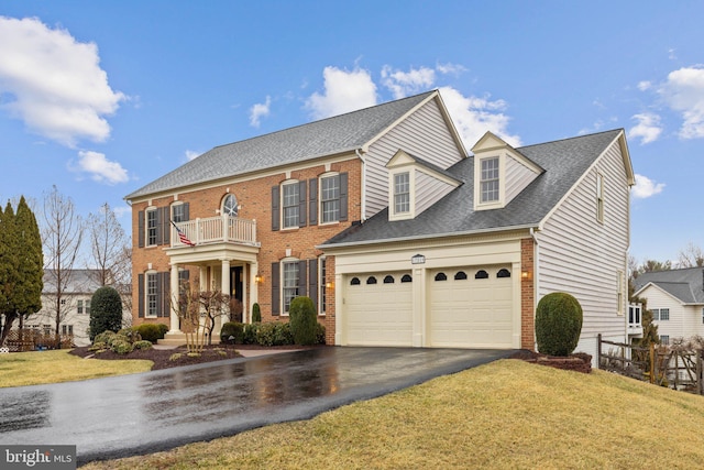 colonial inspired home featuring driveway, a garage, brick siding, a balcony, and a front yard