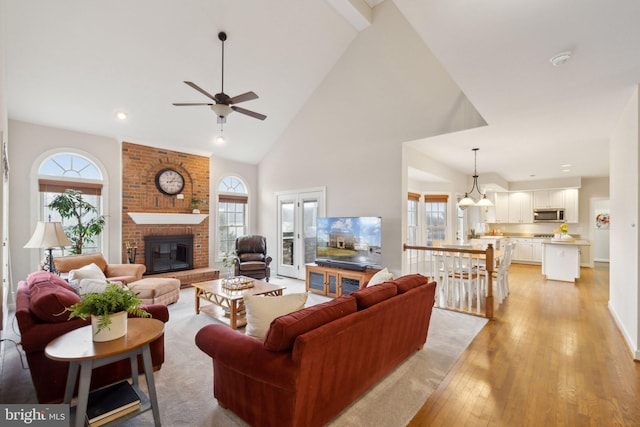 living room with high vaulted ceiling, a fireplace, plenty of natural light, and light wood-style flooring