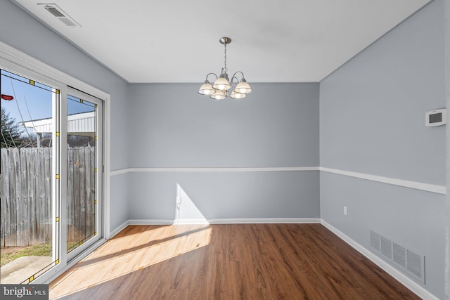 empty room with a chandelier, wood finished floors, visible vents, and baseboards