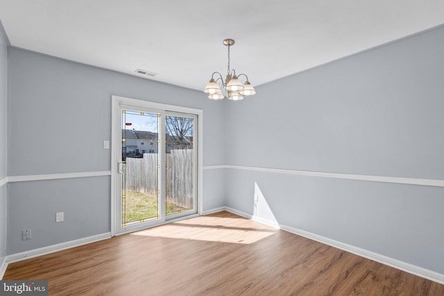 unfurnished dining area with visible vents, a notable chandelier, baseboards, and wood finished floors