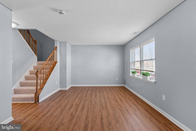 empty room with stairs, baseboards, and wood finished floors