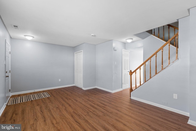 unfurnished room featuring baseboards, visible vents, stairway, and wood finished floors