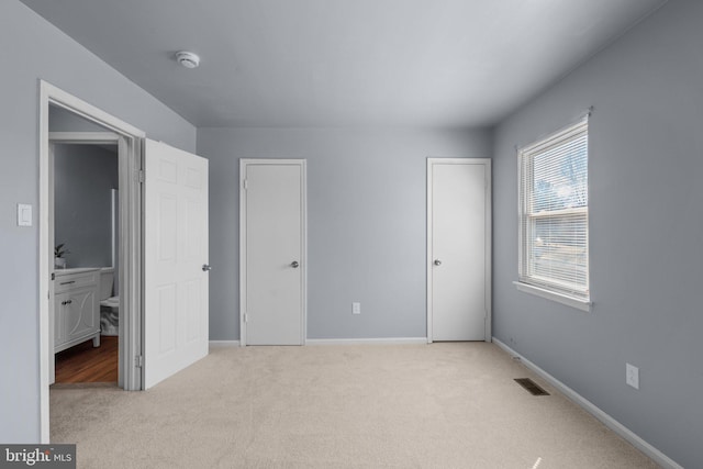 unfurnished bedroom featuring light carpet, two closets, visible vents, and baseboards