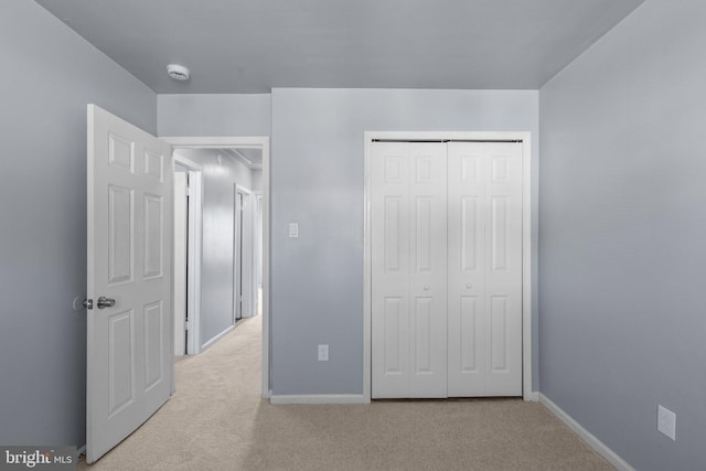 unfurnished bedroom featuring light carpet, baseboards, and a closet