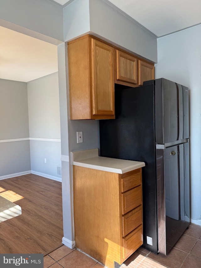 kitchen with light countertops, visible vents, freestanding refrigerator, baseboards, and tile patterned floors