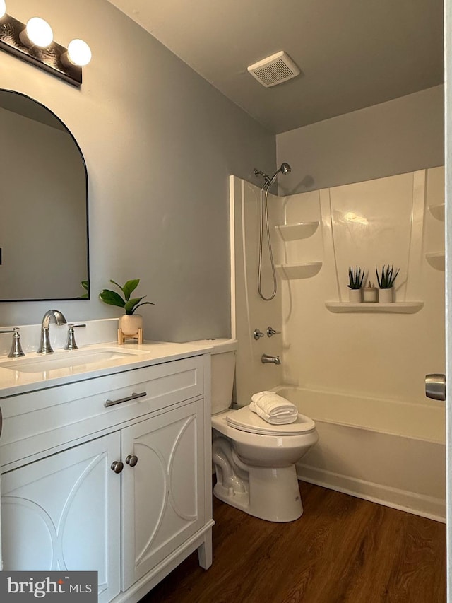 bathroom featuring toilet, wood finished floors, vanity, visible vents, and washtub / shower combination