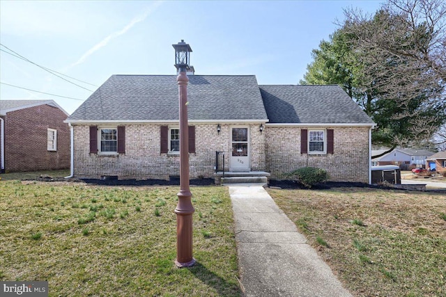 view of front of house featuring brick siding, a front yard, and roof with shingles