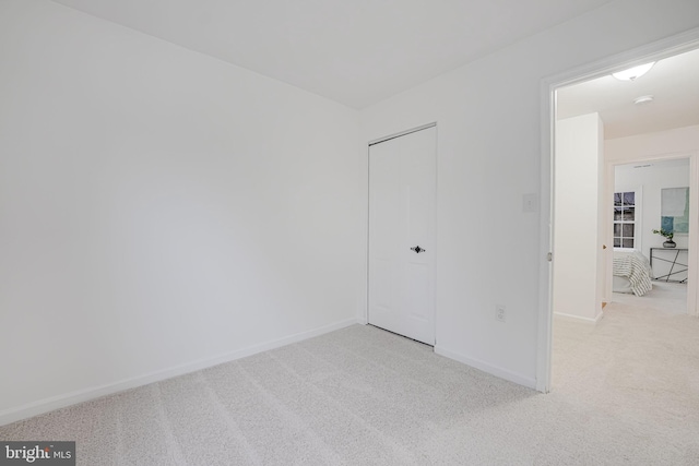 unfurnished bedroom with a closet, light colored carpet, and baseboards