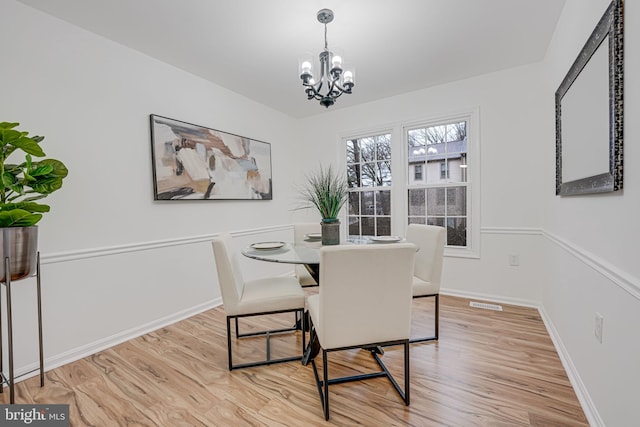 dining room with baseboards, a notable chandelier, visible vents, and light wood finished floors