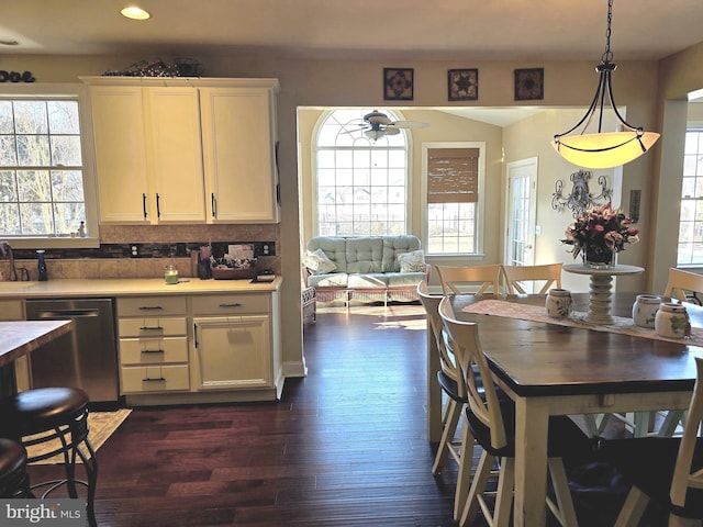 kitchen with a ceiling fan, light countertops, stainless steel dishwasher, hanging light fixtures, and dark wood-style floors