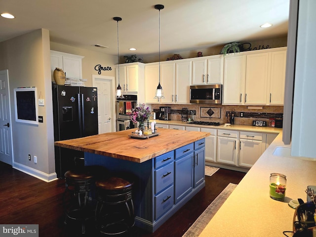 kitchen with cooktop, stainless steel microwave, decorative backsplash, white cabinets, and butcher block countertops