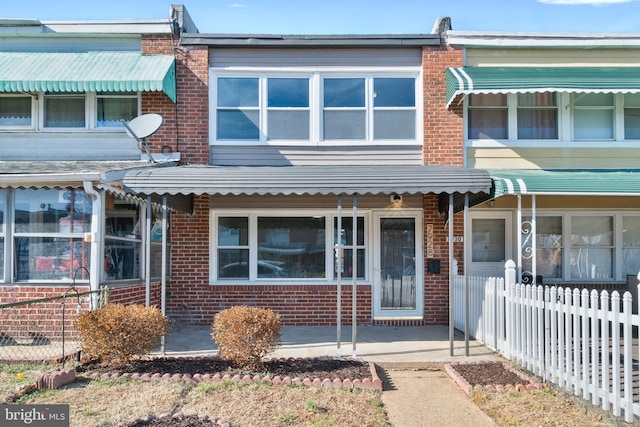 view of front of home featuring brick siding, a porch, and fence